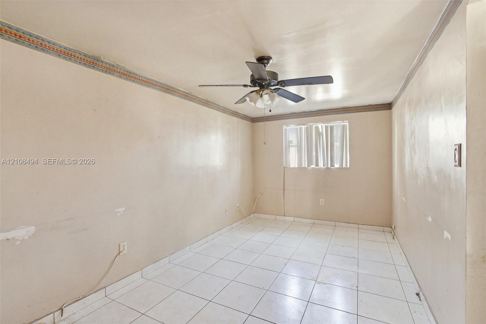 Interior room featuring light-toned tile flooring, decorative crown molding, and a central ceiling fan with an integrated light fixture
