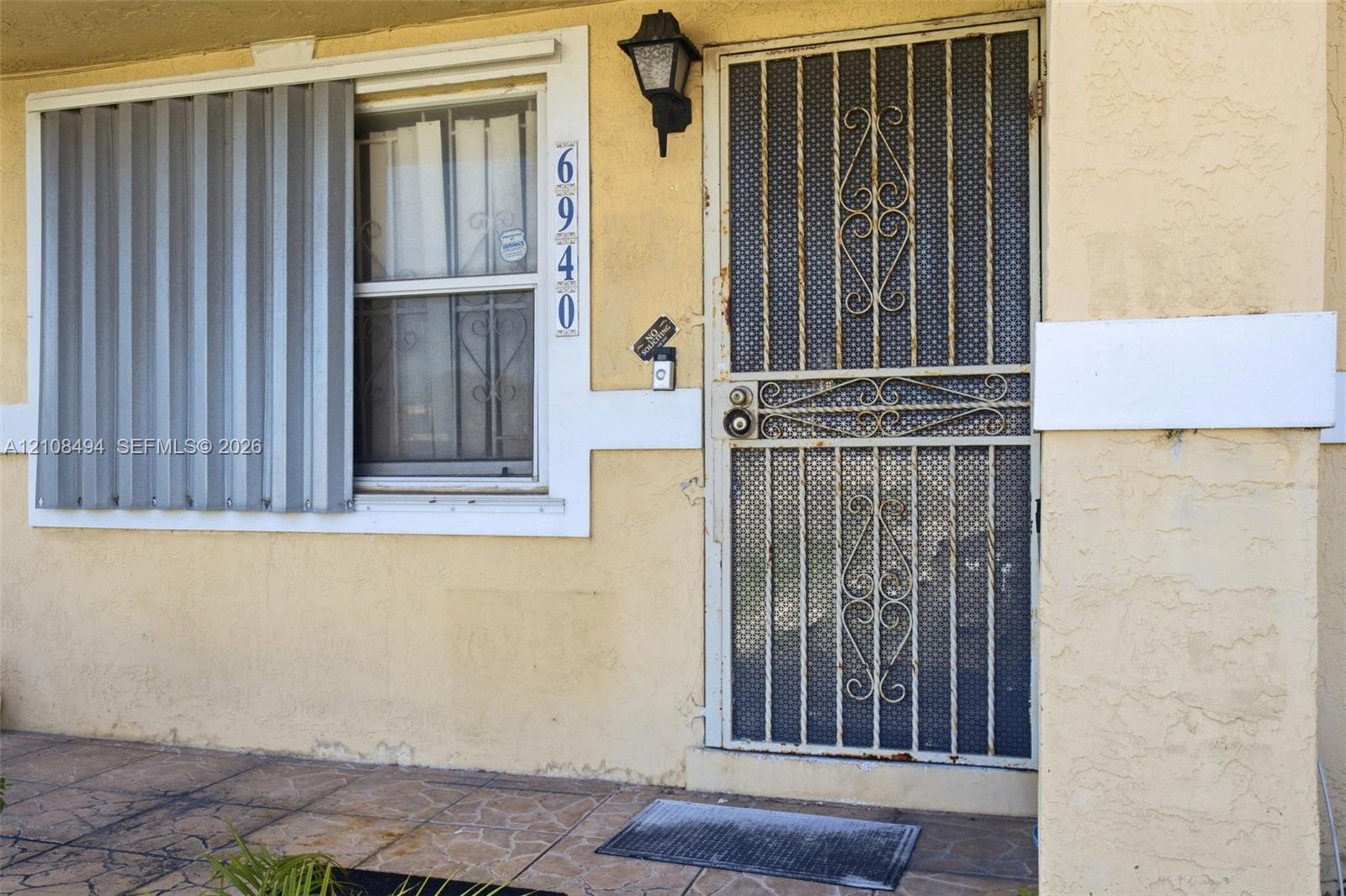 Stucco exterior entry featuring a decorative metal screen door, exterior storm shutters, and tiled porch flooring Stucco exterior entry featuring a decorative metal screen door, exterior storm shutters, and tiled porch flooring