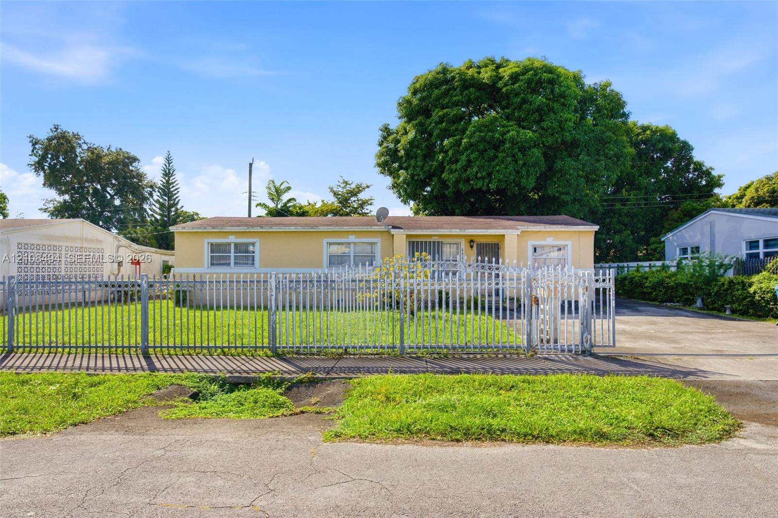 Single-story residence featuring a stucco exterior, concrete driveway, metal picket fencing, and mature trees Single-story residence featuring a stucco exterior, concrete driveway, metal picket fencing, and mature trees
