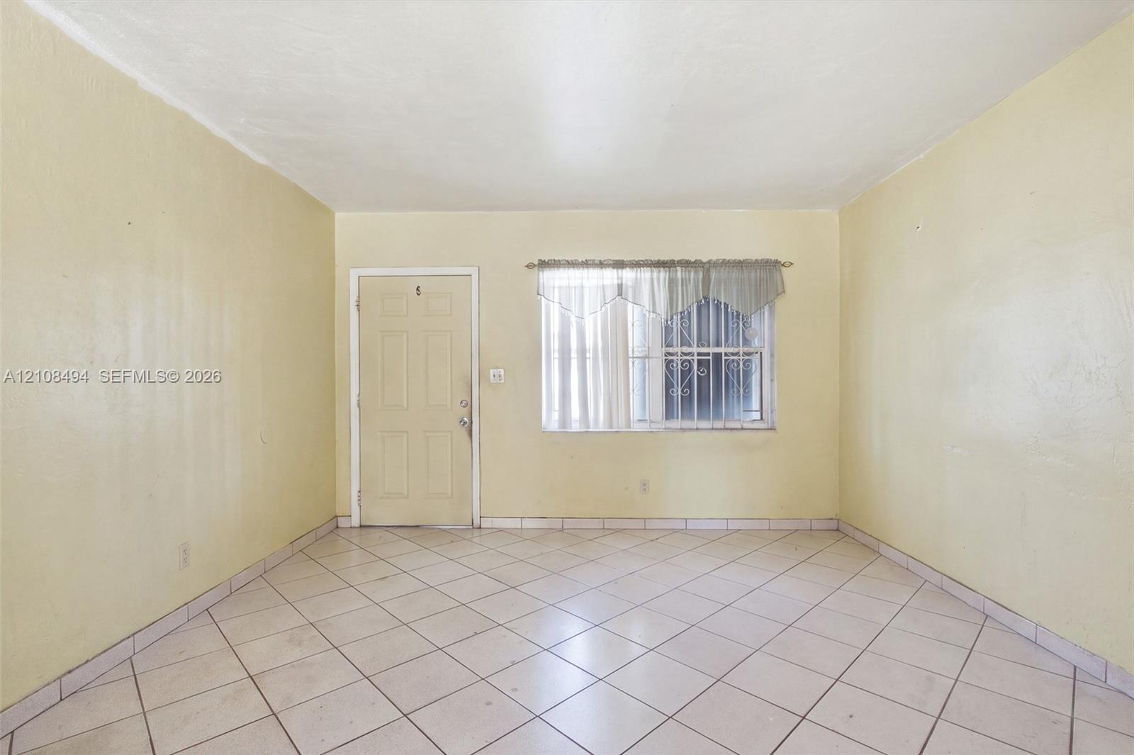 Interior space featuring diagonal ceramic tile flooring, a six-panel exterior entry door, and a window with security bars Interior space featuring diagonal ceramic tile flooring, a six-panel exterior entry door, and a window with security bars
