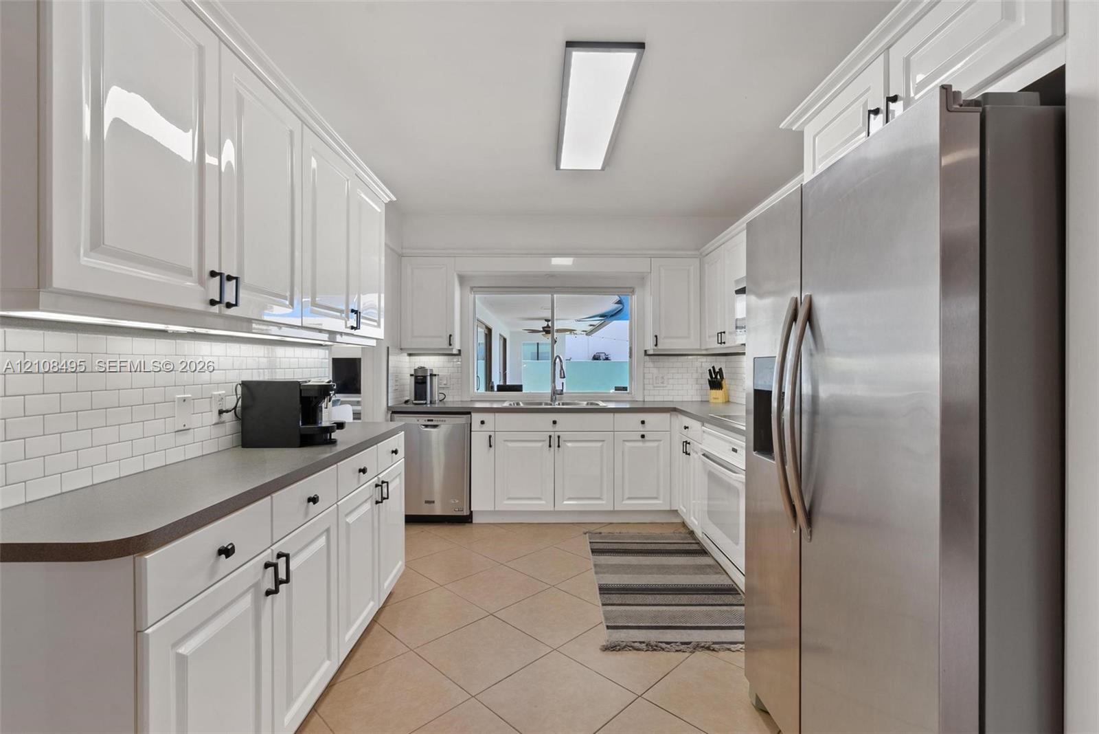 Kitchen featuring white shaker-style cabinetry, matte black hardware, white subway tile backsplash, solid-surface countertops, and stainless steel appliances