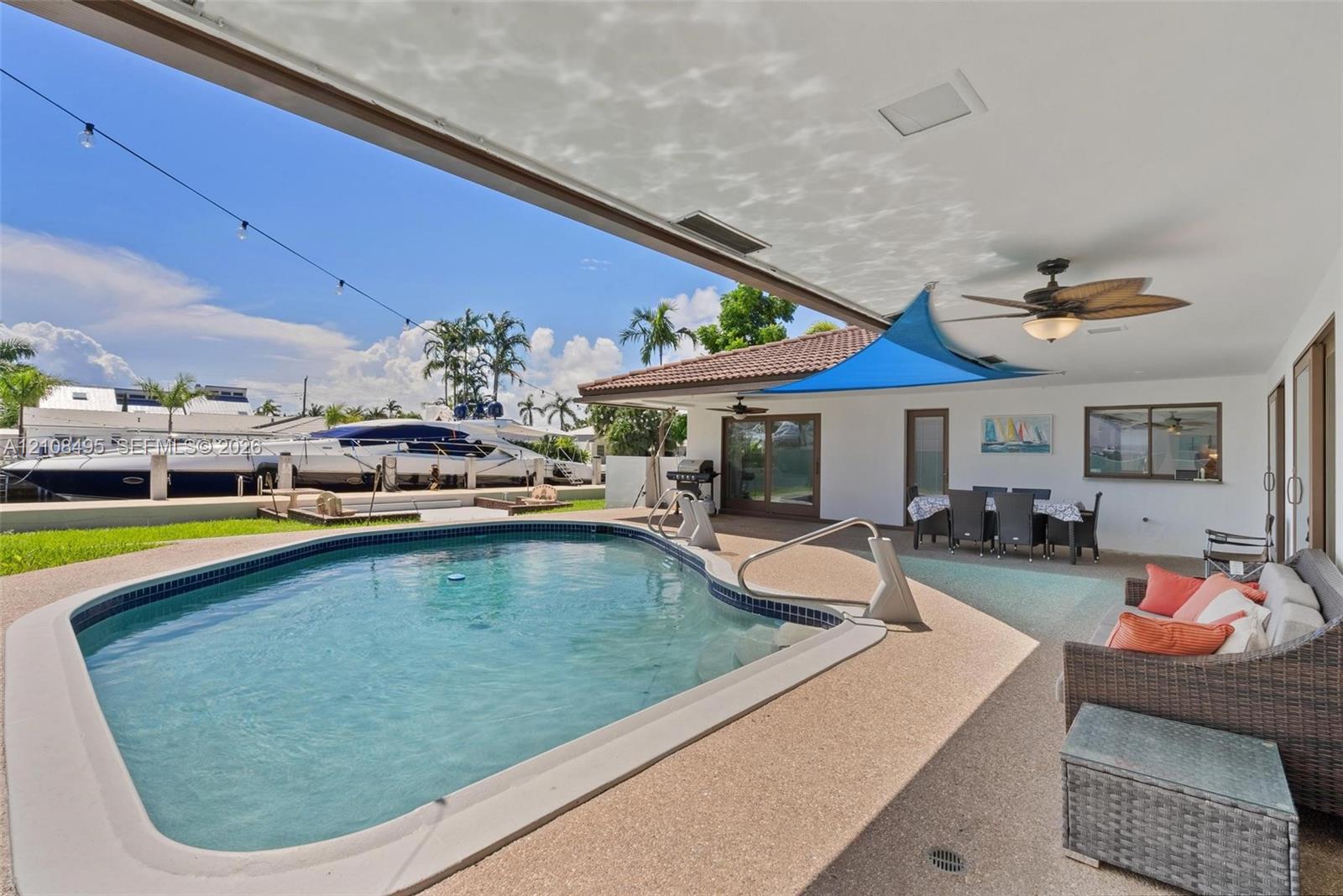 Covered outdoor patio with a ceiling fan, concrete pool deck, and an inground swimming pool with water access