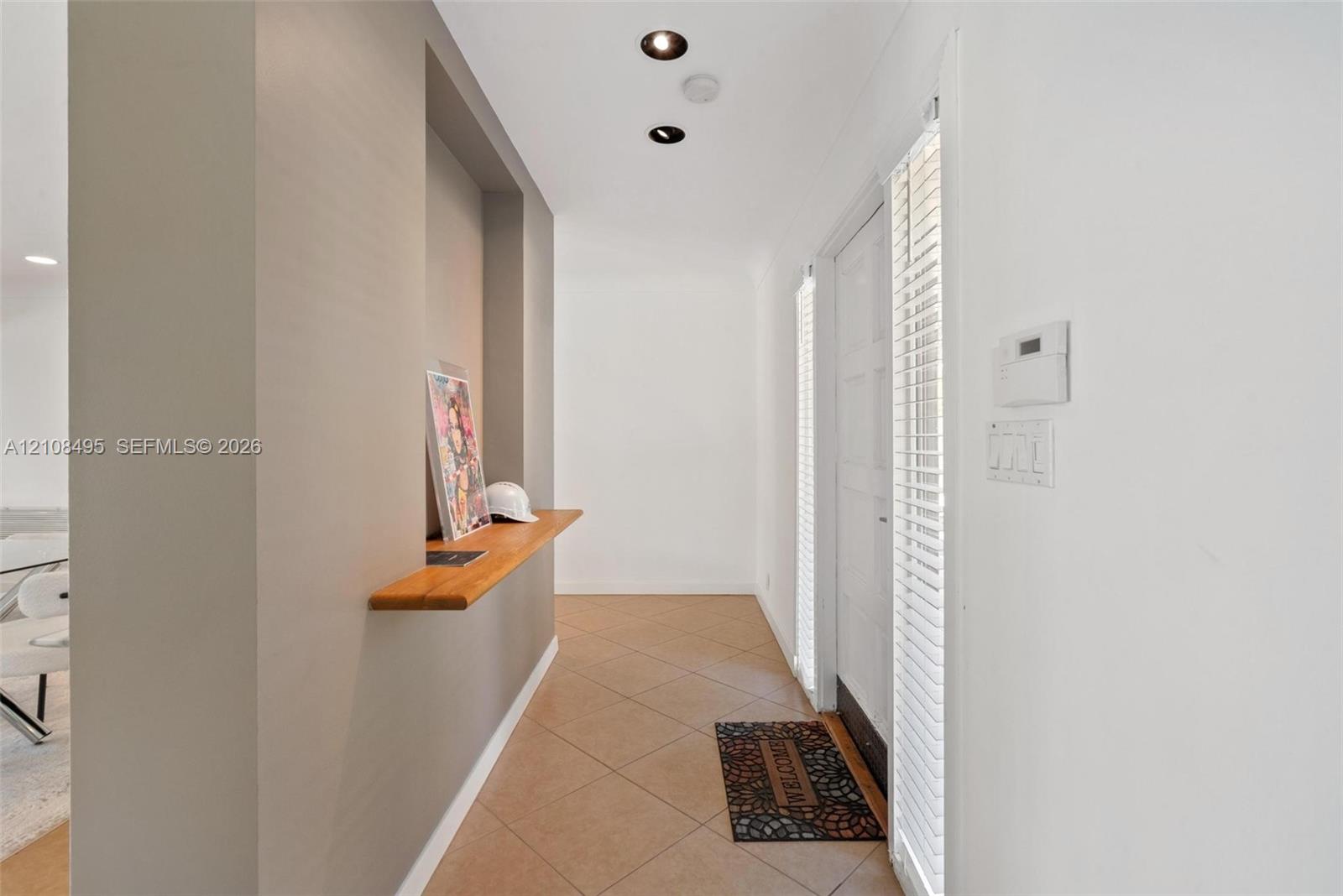 Entryway featuring a built-in wood-finish display shelf, recessed ceiling lighting, tile flooring, and vertical blinds