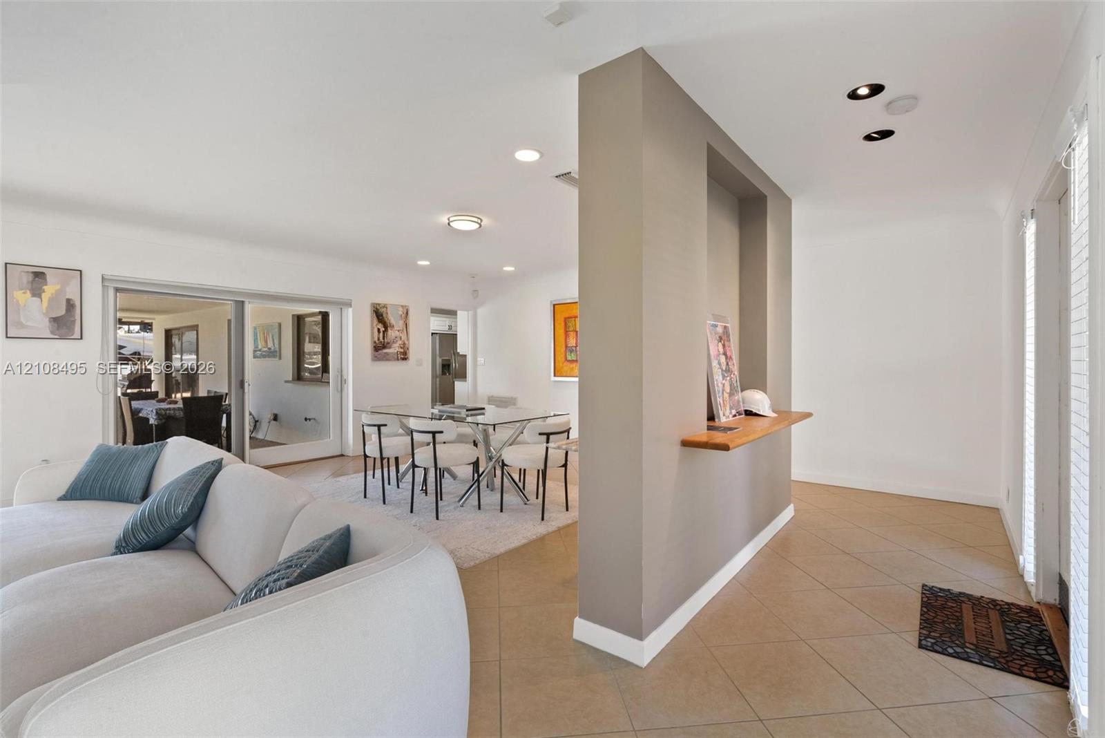 Open-concept living space featuring large-format diagonal tile flooring, a central partition wall with a recessed display niche and built-in wood shelf, recessed ceiling lighting, and sliding glass doors