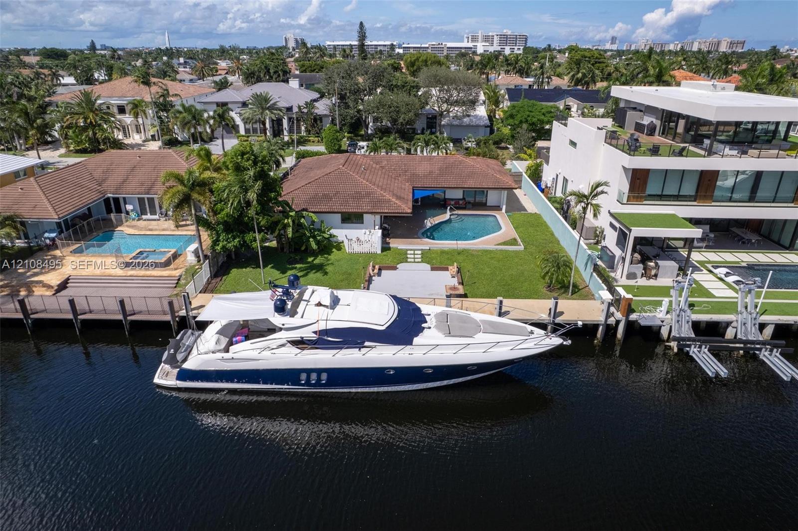 Waterfront property featuring a private boat dock, concrete seawall, in-ground swimming pool, and manicured lawn