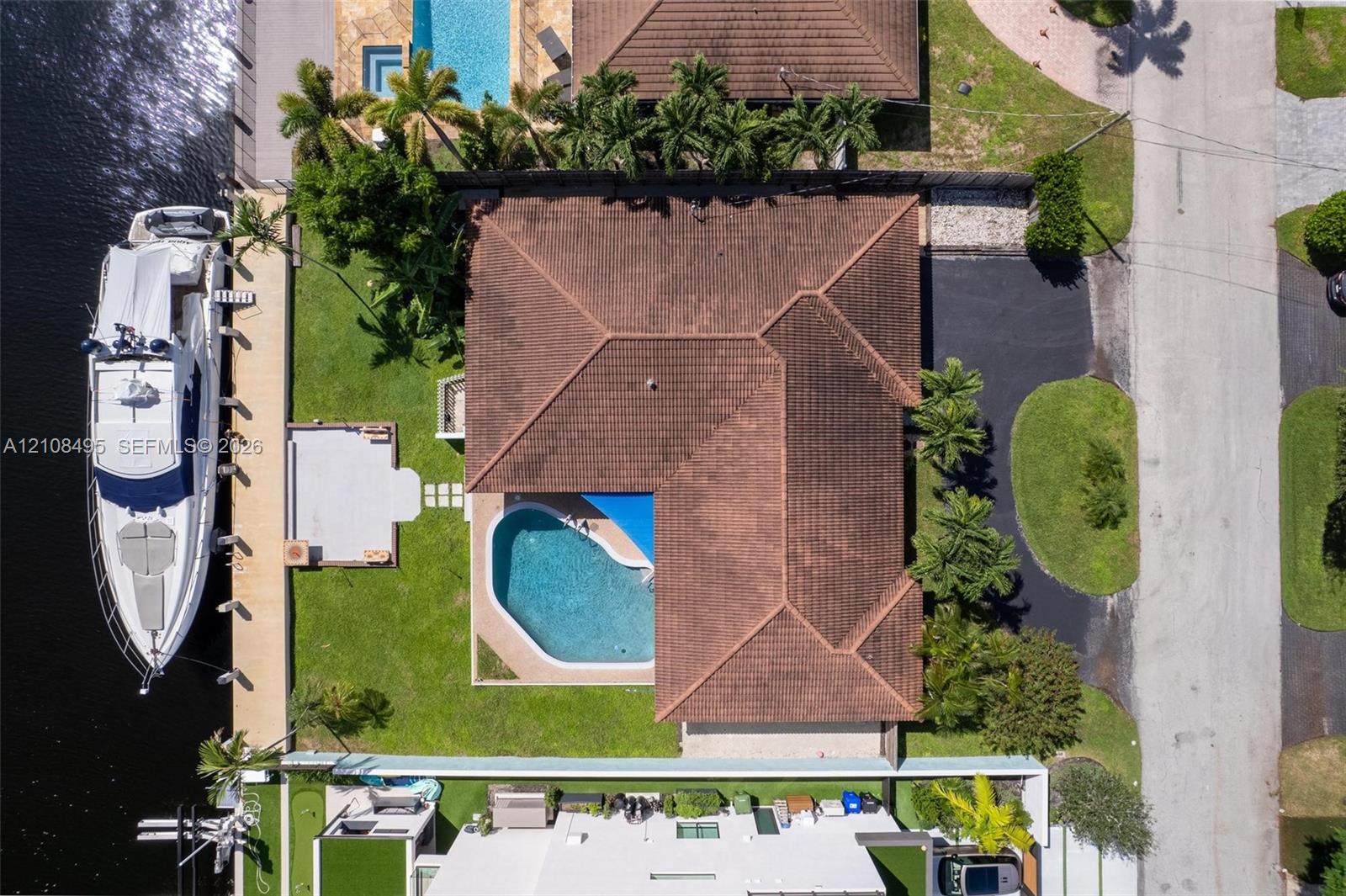 Aerial view of a waterfront property featuring a private boat dock, a swimming pool, a tiled roof, and a paved driveway
