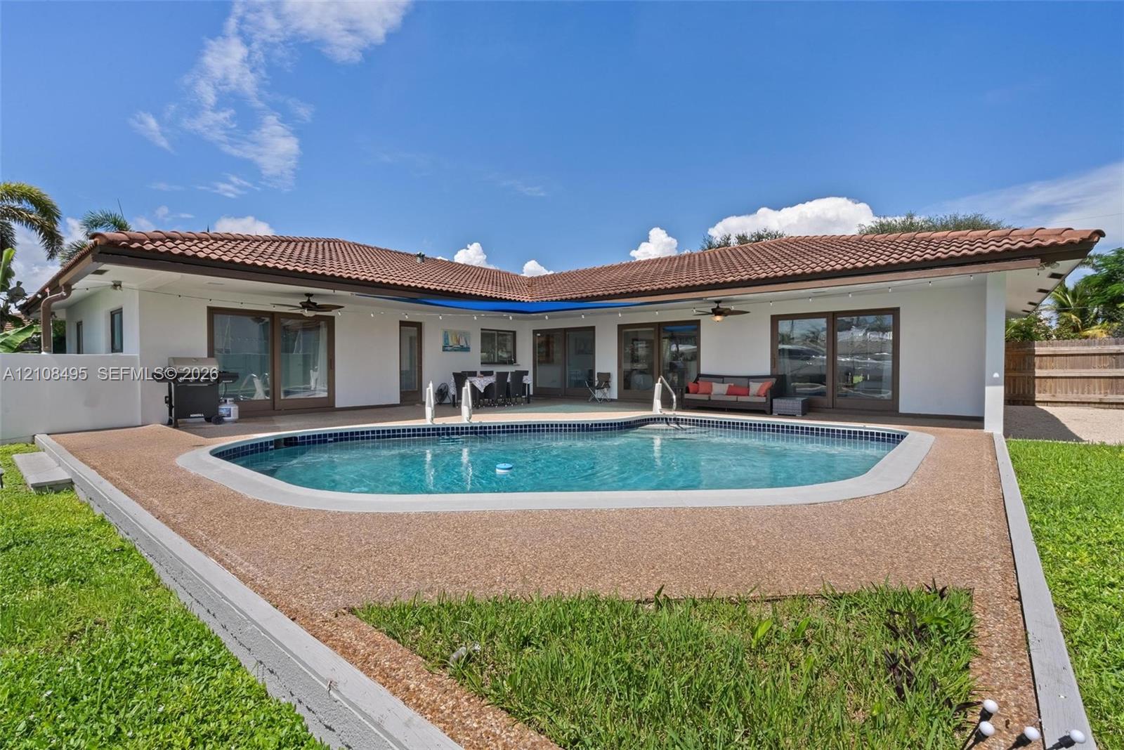L-shaped exterior featuring a tiled roof, in-ground swimming pool with aggregate decking, and multiple sliding glass door entries