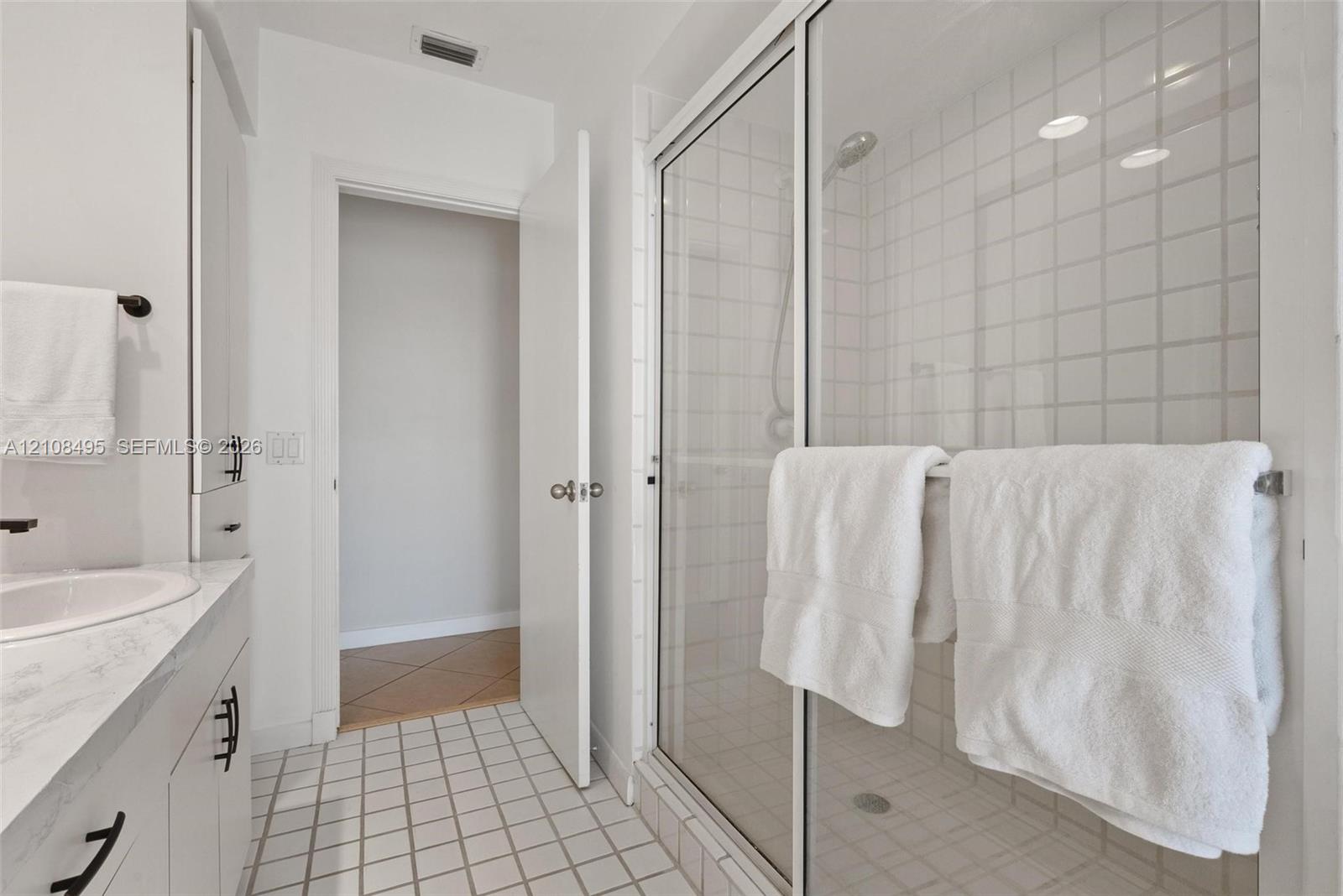 Bathroom featuring a vanity with a white countertop and integrated sink, a glass-enclosed shower with tiled surround, and a tall built-in storage cabinet with matte black hardware