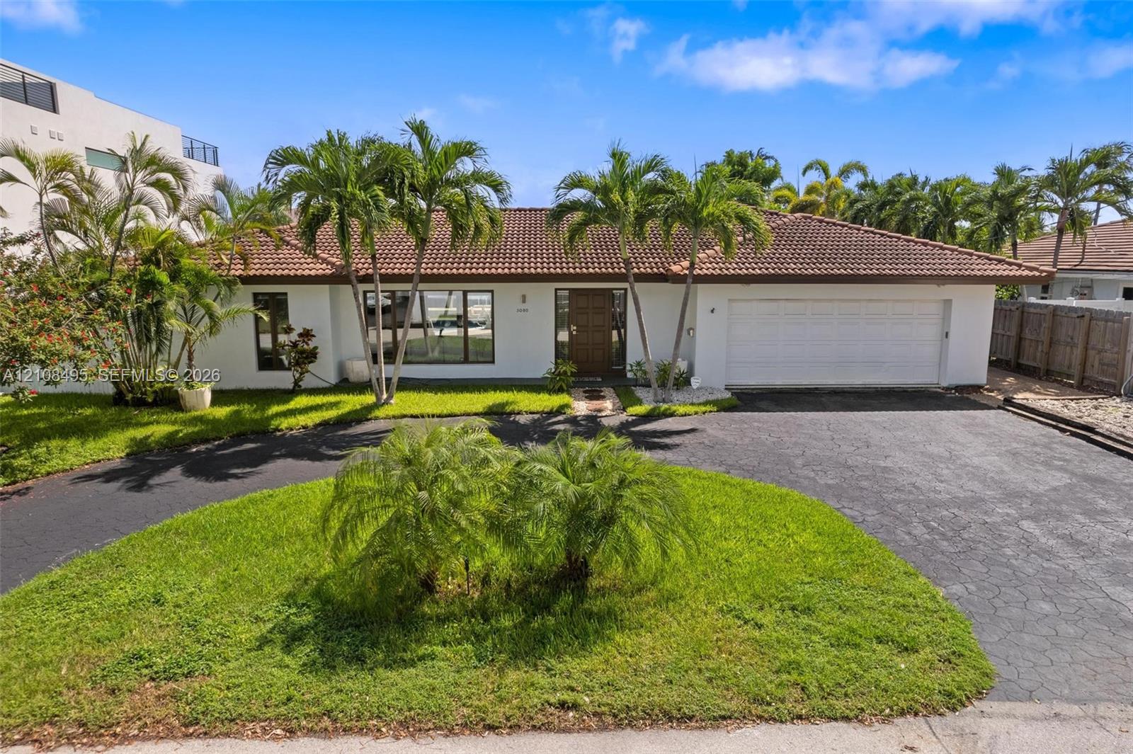 Single-story exterior featuring white stucco siding, a tiled roof, a multi-car garage, and a paved circular driveway Single-story exterior featuring white stucco siding, a tiled roof, a multi-car garage, and a paved circular driveway