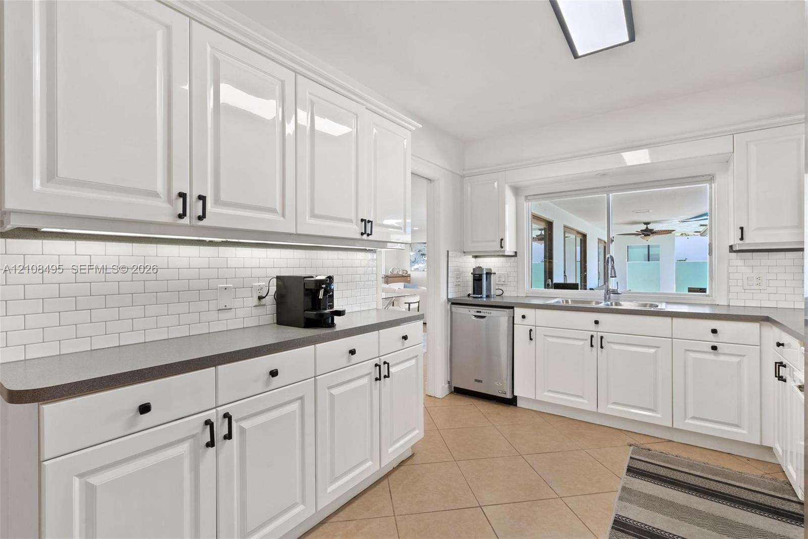 Kitchen featuring white cabinetry, subway tile backsplash, solid-surface countertops, stainless steel dishwasher, and tile flooring