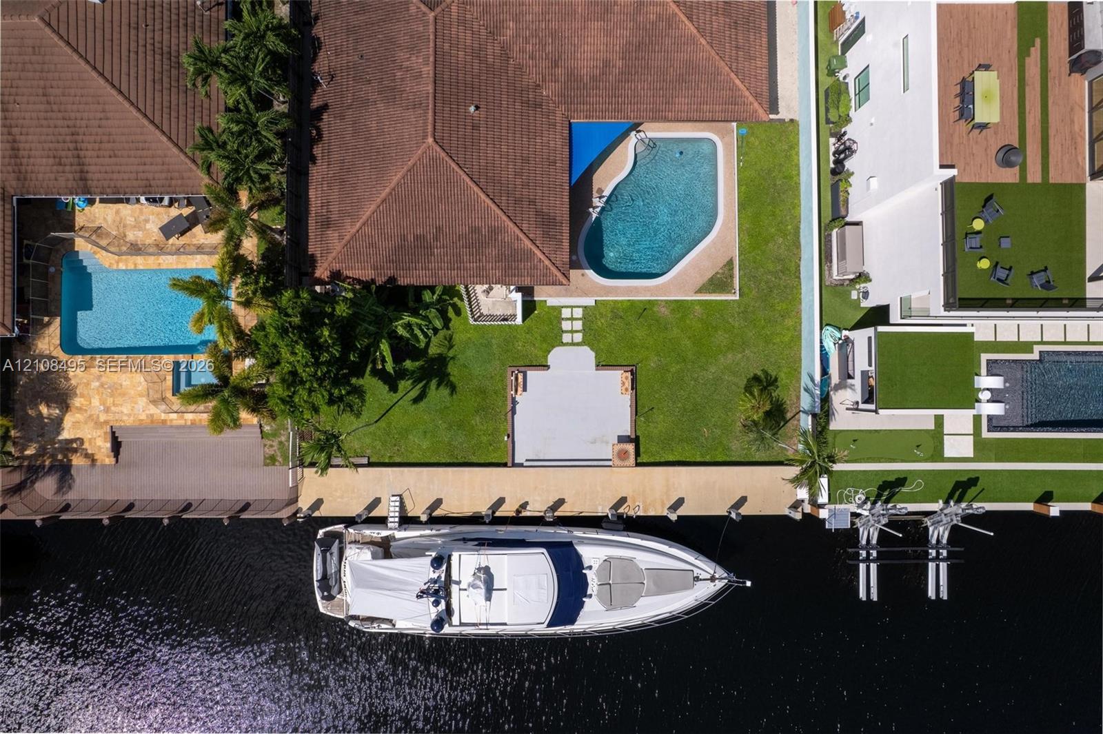 Waterfront property featuring a private concrete dock, an in-ground swimming pool, a sodded lawn, and a paved patio area
