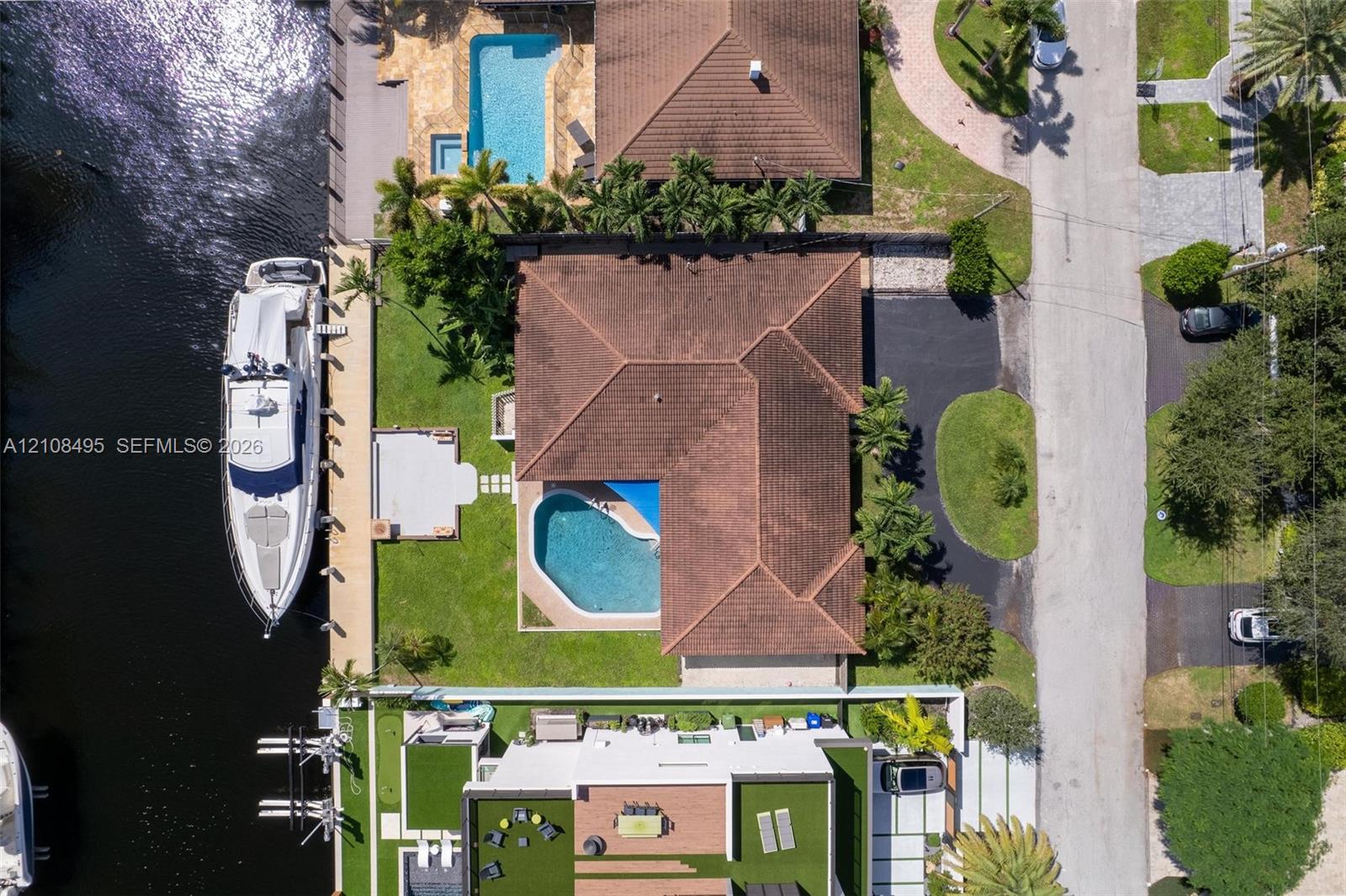 Aerial perspective of a waterfront property featuring a canal-front bulkhead, private swimming pool, concrete patio, paved driveway, and tile roof