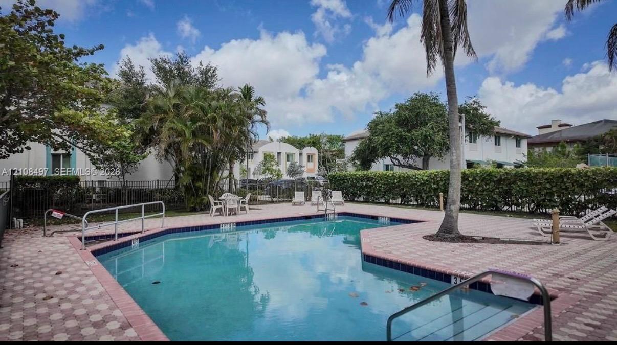 Swimming pool with a paved deck, perimeter hedging, and metal fencing