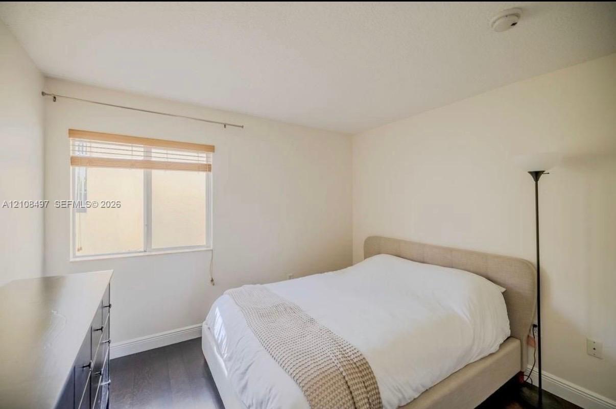 Room featuring dark wood-finish flooring, neutral wall tones, and a single-pane sliding window with horizontal slat blinds