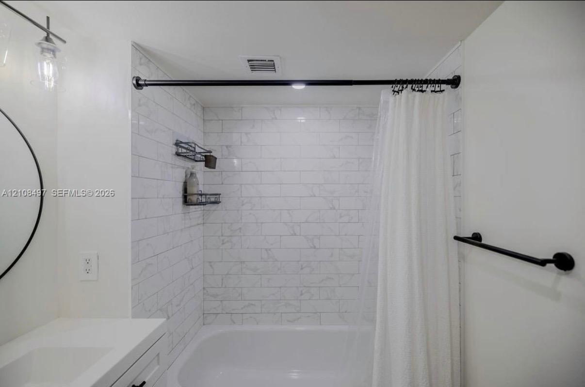 Full bathroom featuring a tub-shower combination with white subway-style tiling, a vanity with a white countertop, a circular wall-mounted mirror, and matte black fixtures