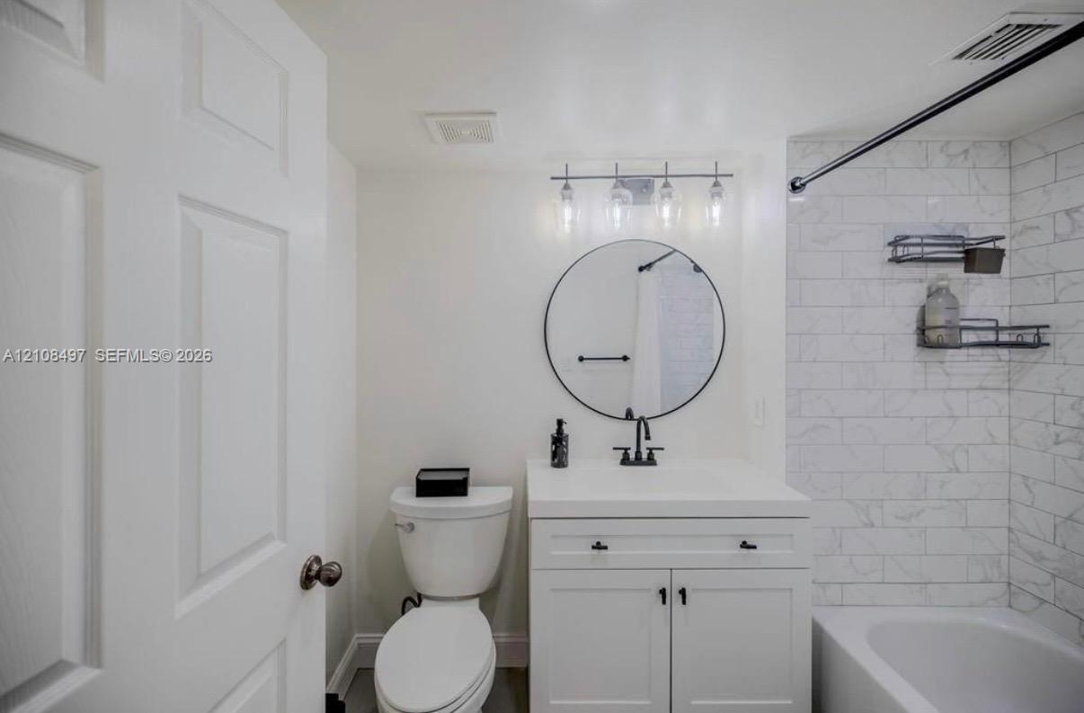 Bathroom featuring a vanity with integrated sink, circular wall-mounted mirror, matte black hardware, and tub surround with subway tile finish