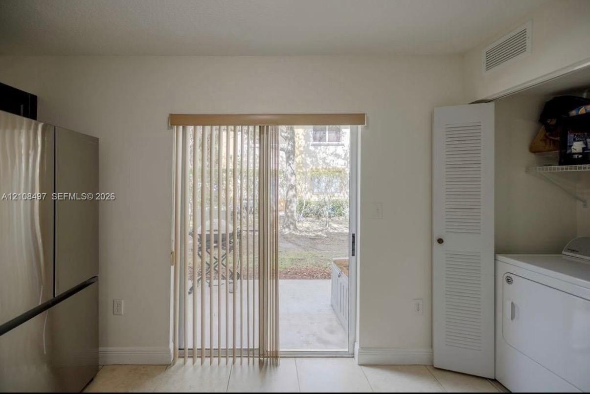 Sliding glass door with vertical blinds, stainless steel refrigerator, louvered closet door, and tile flooring