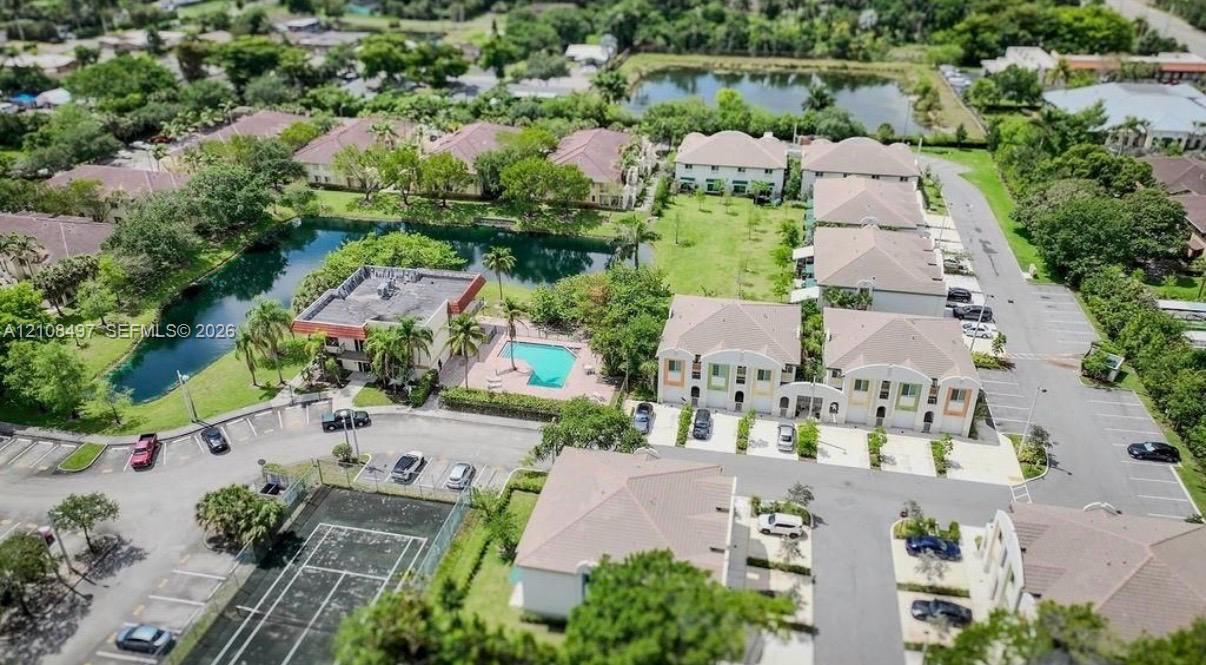 Aerial view featuring a paved tennis court, outdoor swimming pool, water feature, and off-street parking area