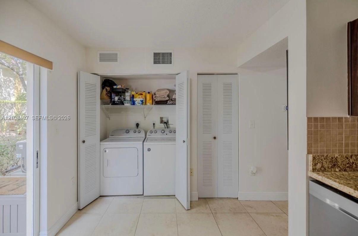 Laundry closet featuring side-by-side appliances, overhead shelving, and louvered folding doors, complemented by tile flooring and an additional louvered-door closet