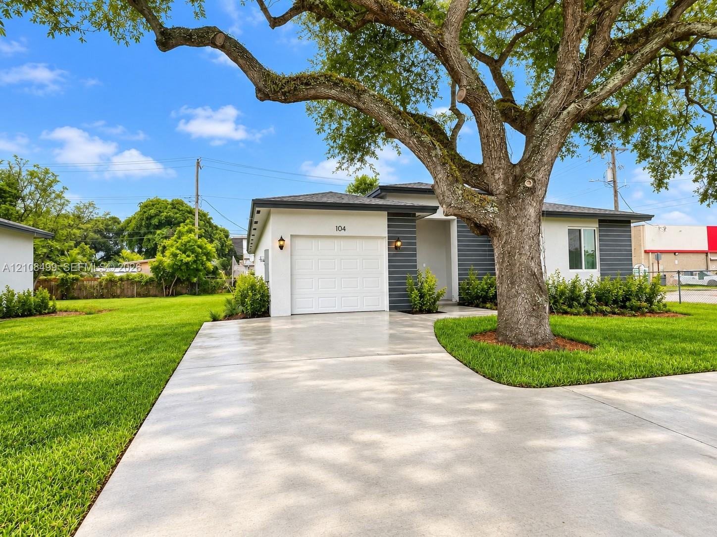 Exterior featuring light-colored stucco, contrasting dark grey horizontal siding, a single-car garage, an expansive lawn, and a mature shade tree