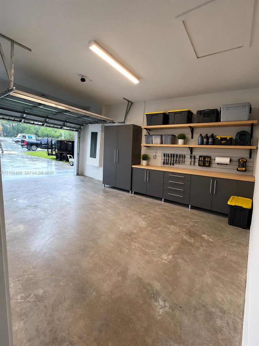Garage featuring custom floor-to-ceiling cabinetry, integrated wall-mounted slat organization, wood-surfaced built-in workbench, and overhead linear lighting