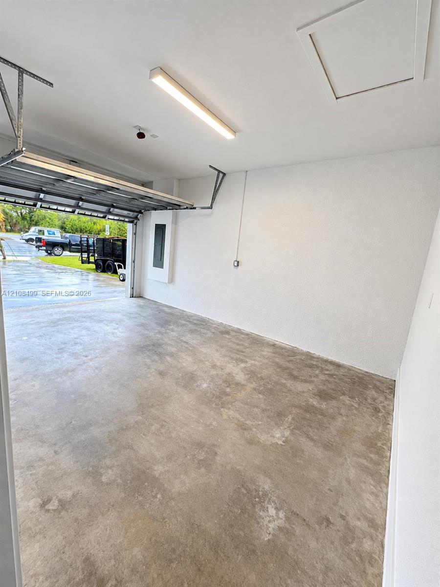 Finished garage featuring smooth-texture walls, a concrete floor, a linear LED light fixture, and an attic access panel
