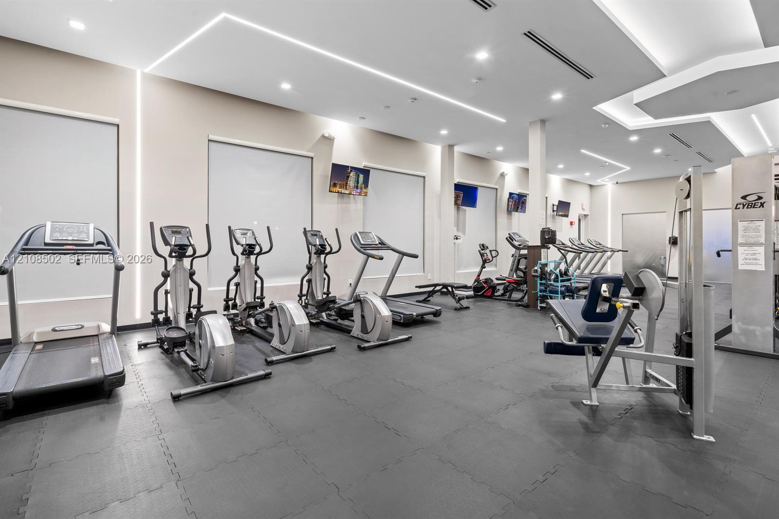 Fitness area featuring recessed ceiling lighting, linear wall-mounted accent illumination, neutral wall finishes, and rubberized flooring