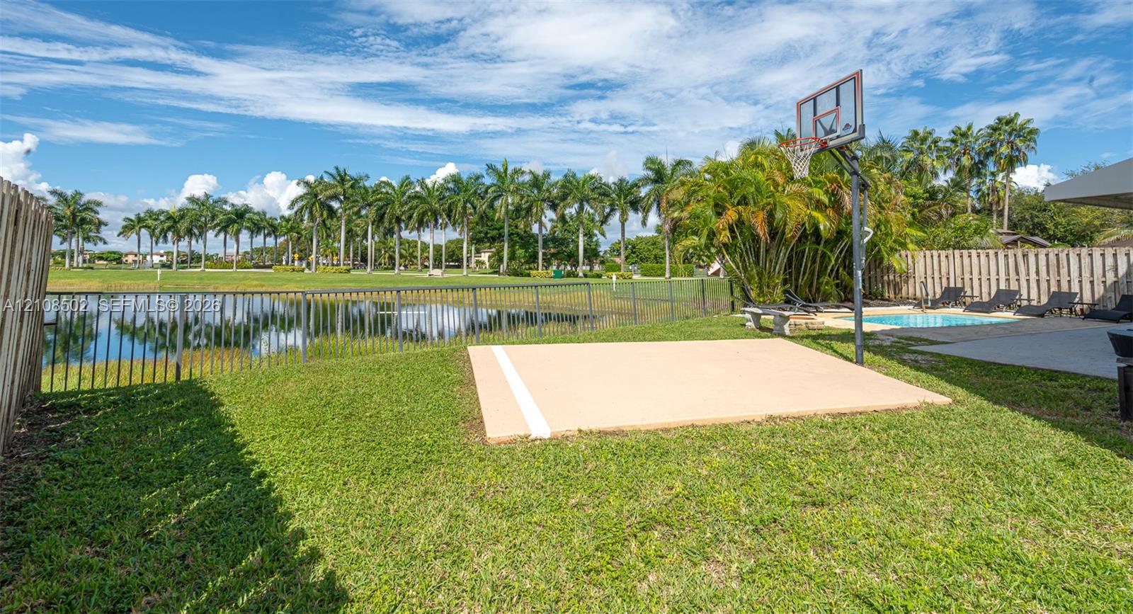 Backyard featuring a paved basketball court, swimming pool, fenced perimeter, and waterfront scenery