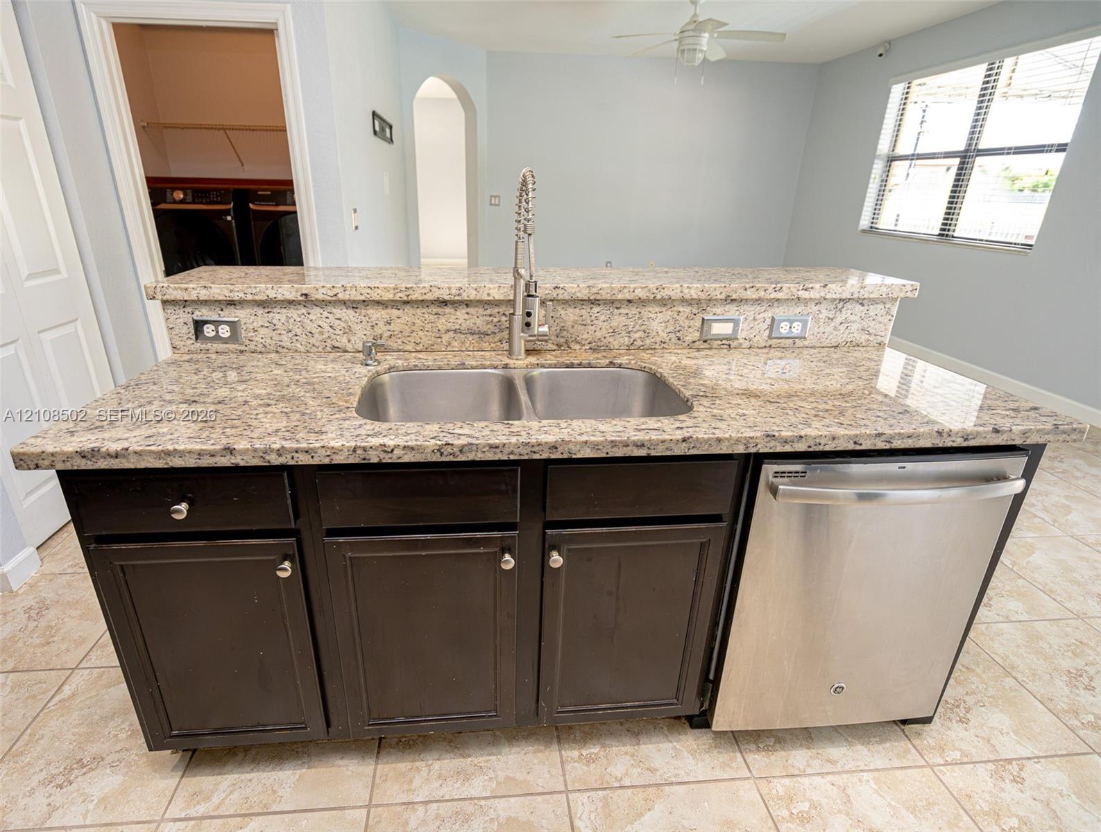 Kitchen island featuring stone countertops, double-basin stainless steel sink with pull-down faucet, dark-finish cabinetry, and stainless steel dishwasher