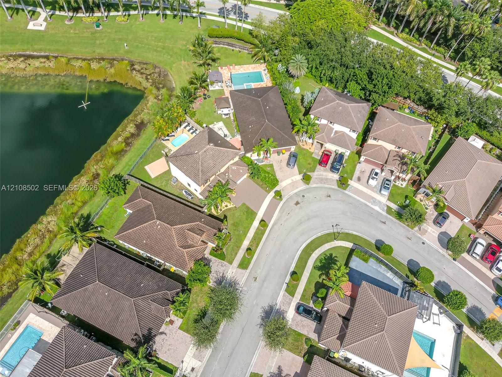 Aerial perspective of a cul-de-sac community featuring waterfront residences, paved driveways, manicured landscaping, and individual swimming pools