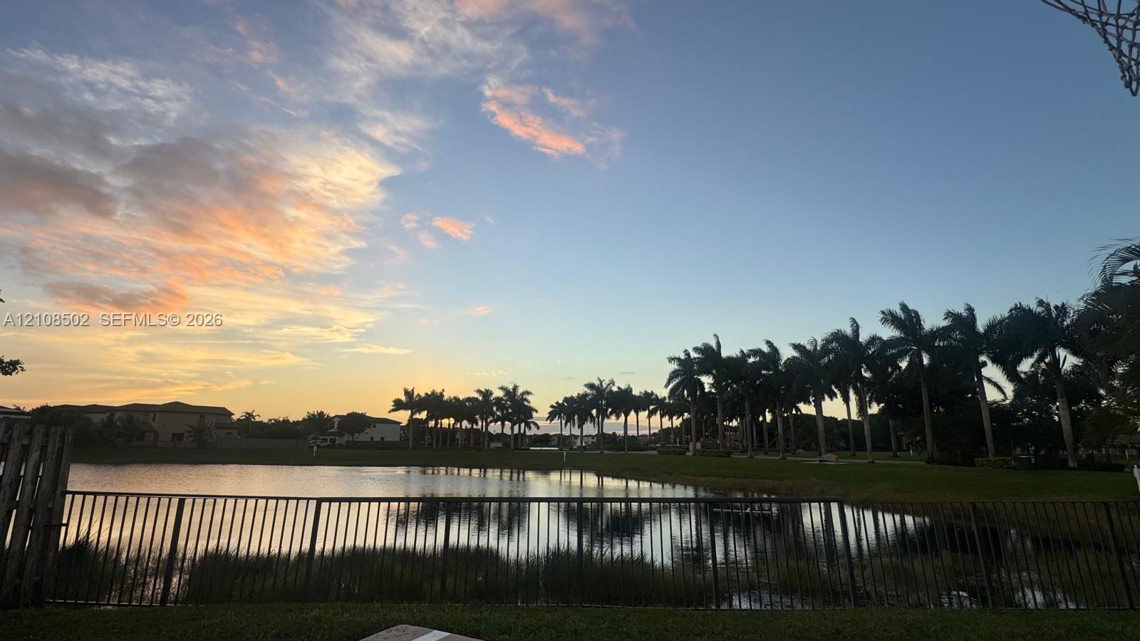 Waterfront property featuring a metal perimeter fence, manicured lawn, and mature palm trees
