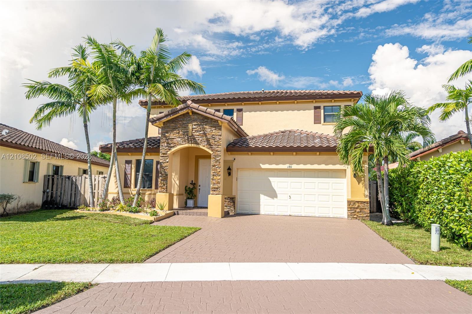Two-story exterior featuring a stone-veneer entryway, tile roof, stucco facade, paved driveway, and mature landscaping