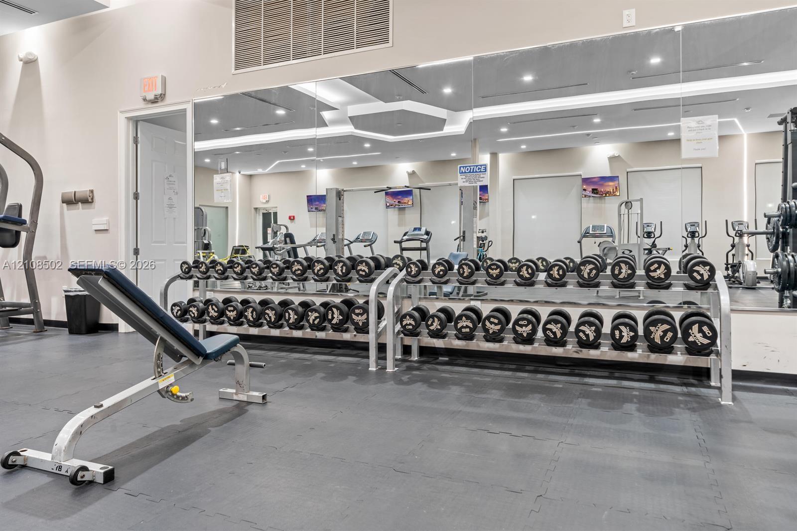 Fitness center featuring industrial-grade rubber flooring, wall-to-wall mirrors, and built-in metal dumbbell racks