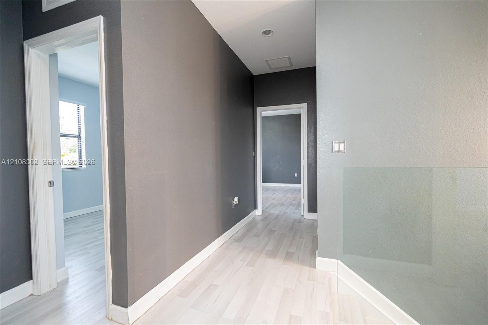 Interior hall featuring wood-finish flooring, two-toned wall paint, recessed lighting, and a minimalist glass panel railing