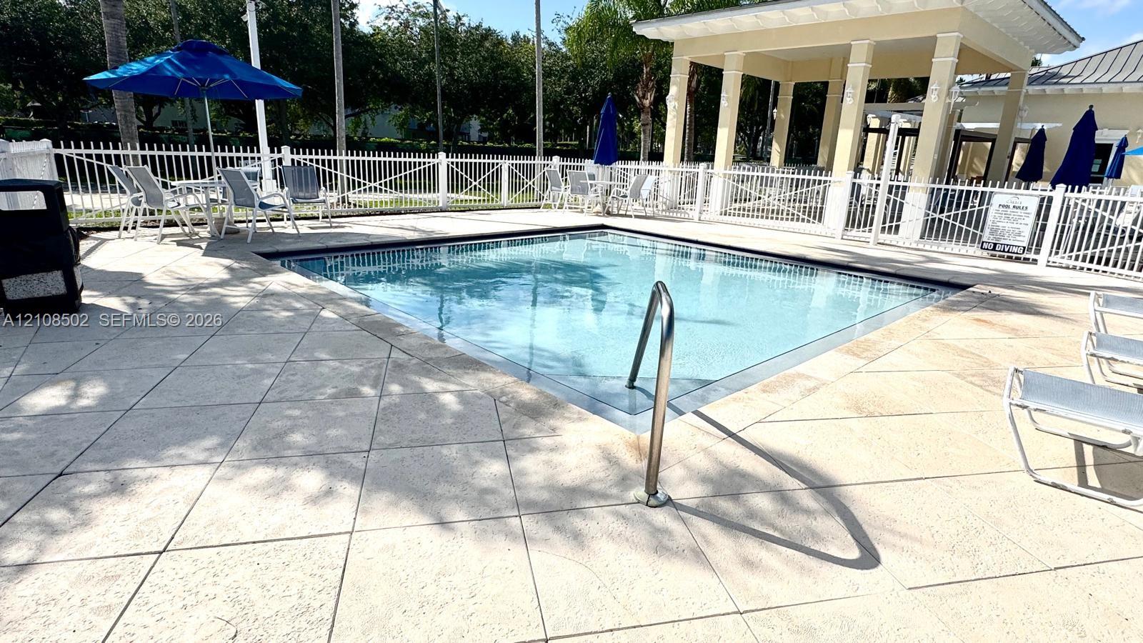 Swimming pool with tile deck surround, metal handrail, and covered pavilion structure enclosed by perimeter fencing