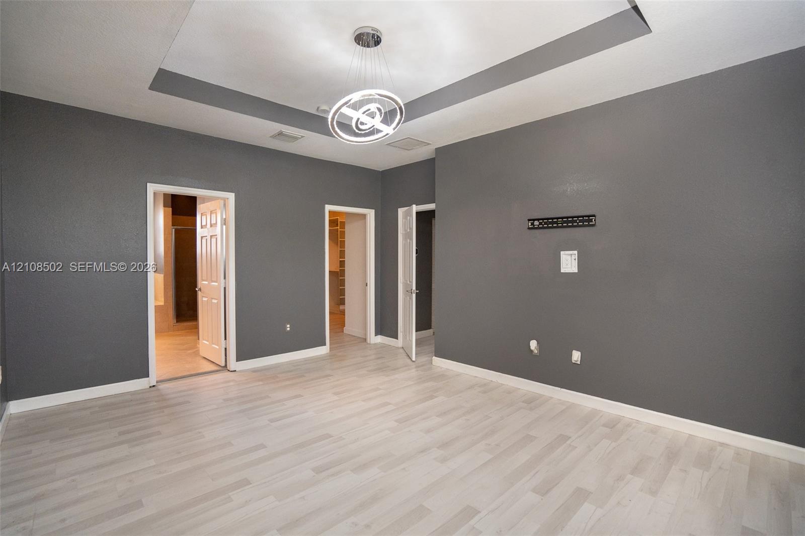 Tray ceiling featuring recessed lighting, light-toned wood-finish flooring, and a modern circular chandelier