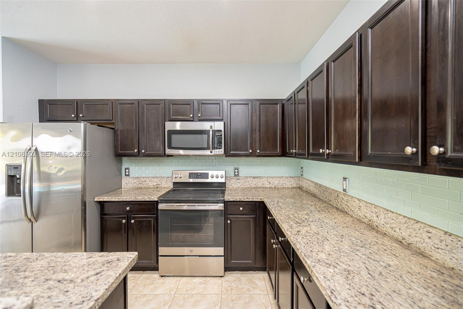 Kitchen featuring dark wood cabinetry, stone countertops, stainless steel appliances, and a light-toned subway tile backsplash
