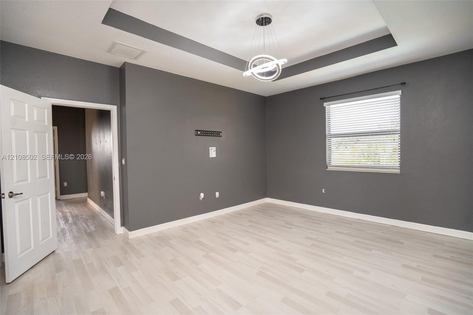 Tray ceiling with integrated lighting, wood-finish flooring, and contemporary circular pendant fixture
