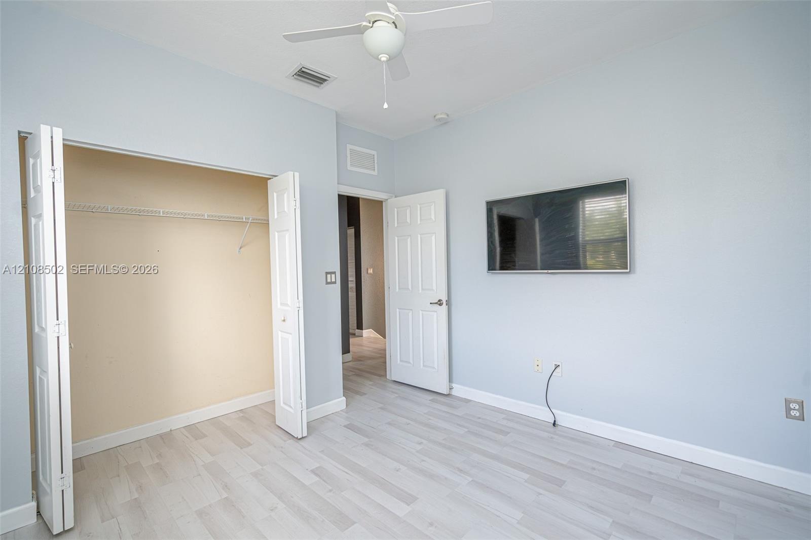 Room featuring wood-finish flooring, a ceiling fan with integrated lighting, and a closet with bifold doors