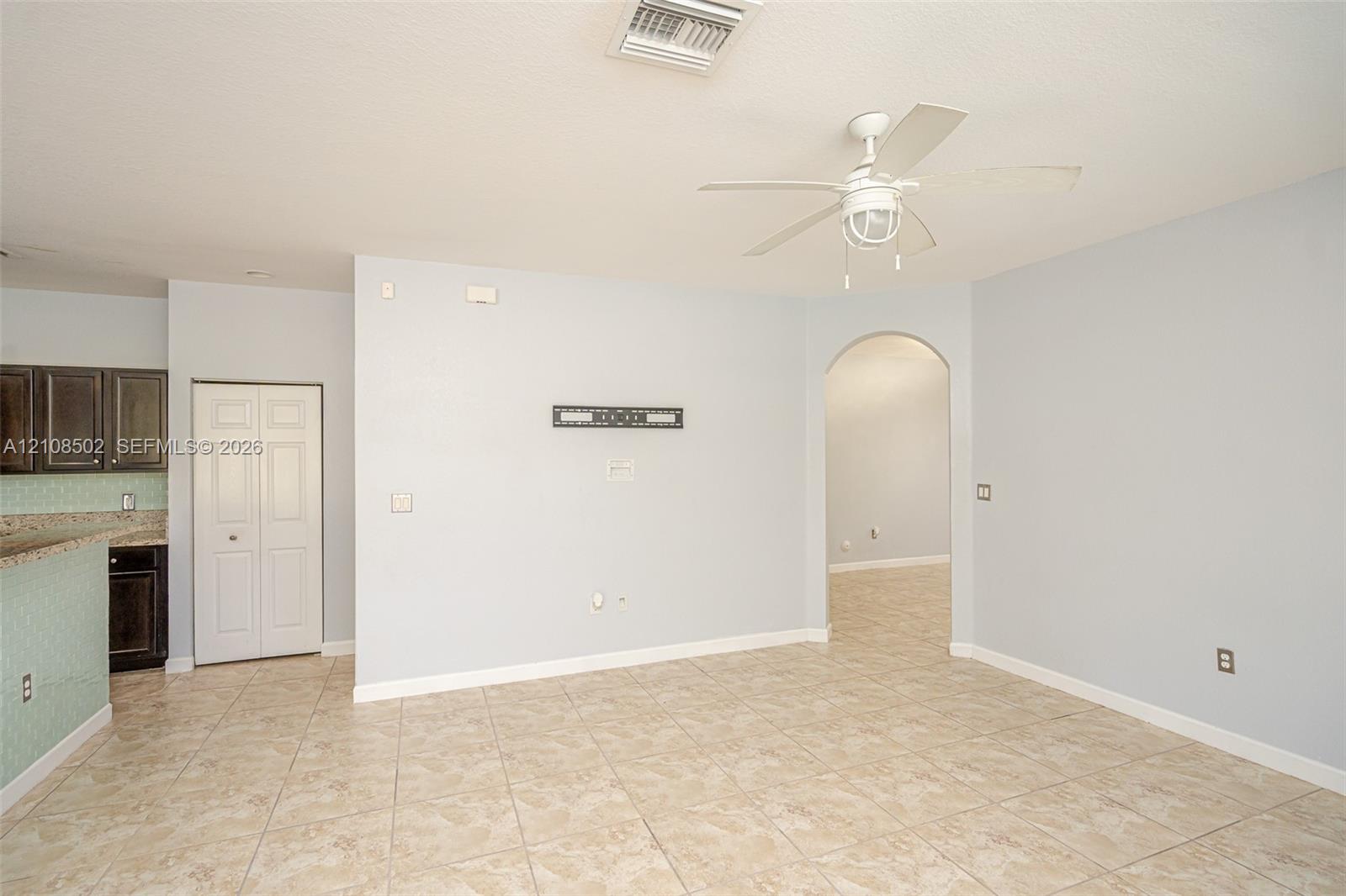 Open interior area featuring tile flooring, a white ceiling fan with integrated lighting, and an arched doorway