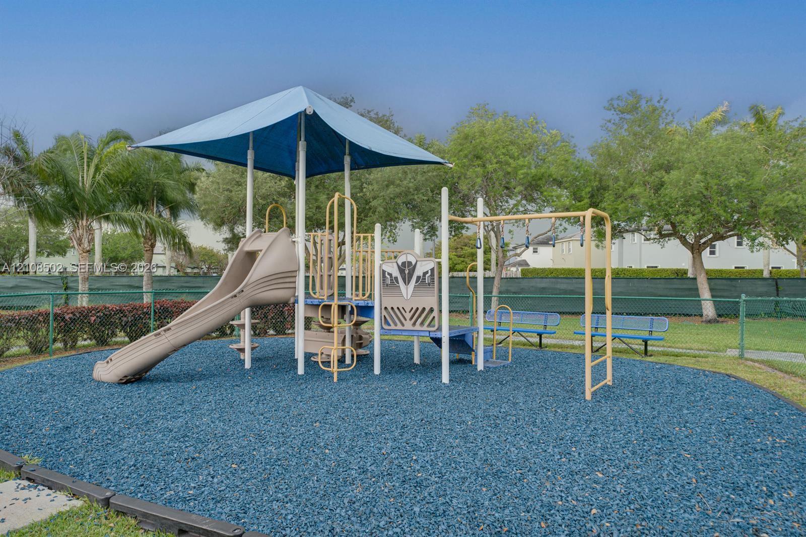 Outdoor recreation area featuring a structured play system with a canopy, integrated slide, and built-in bench seating, all set within a landscaped perimeter