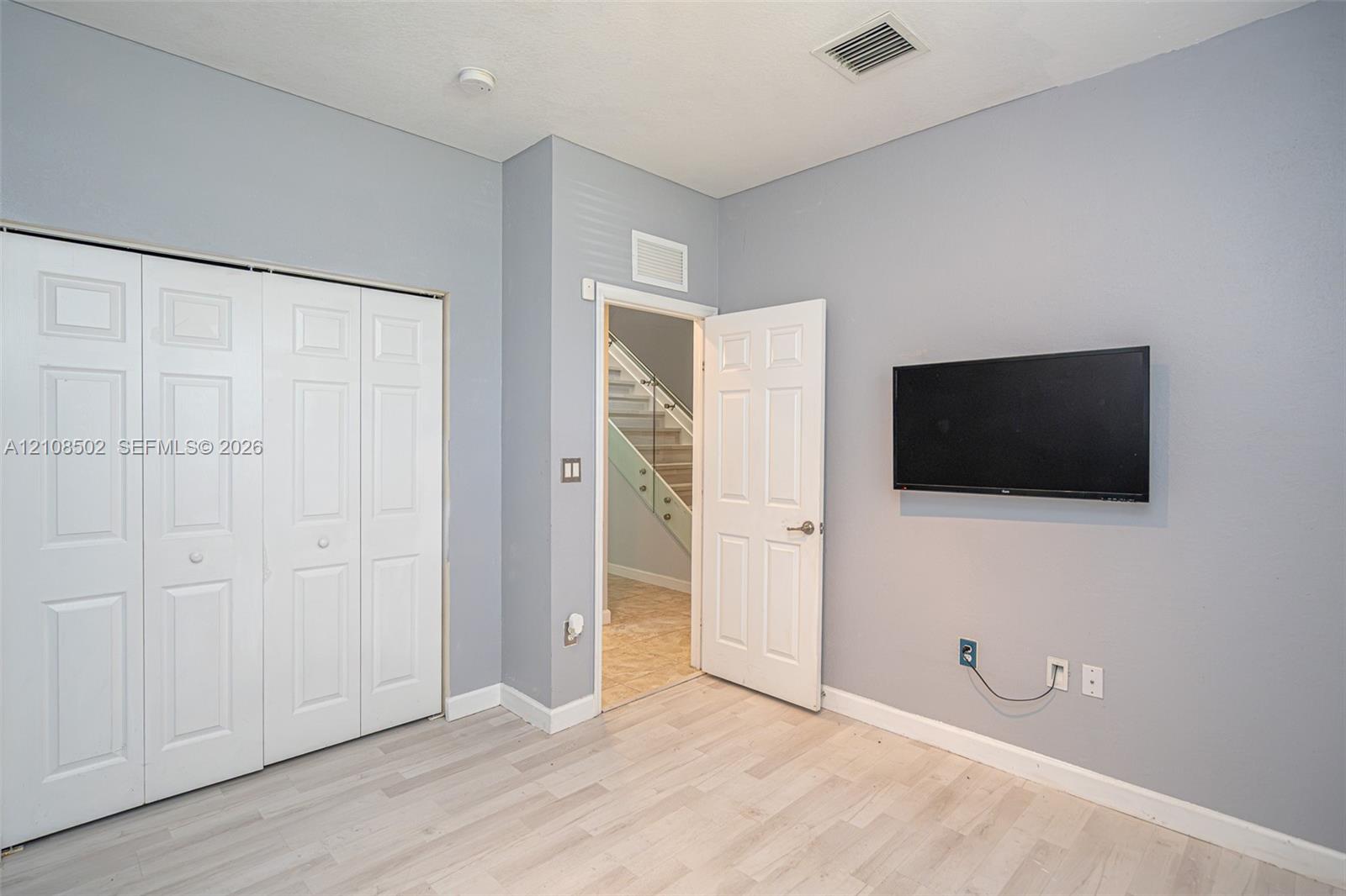 Neutral-toned interior space featuring light wood-finish flooring, four-panel closet doors, and solid-core interior doors