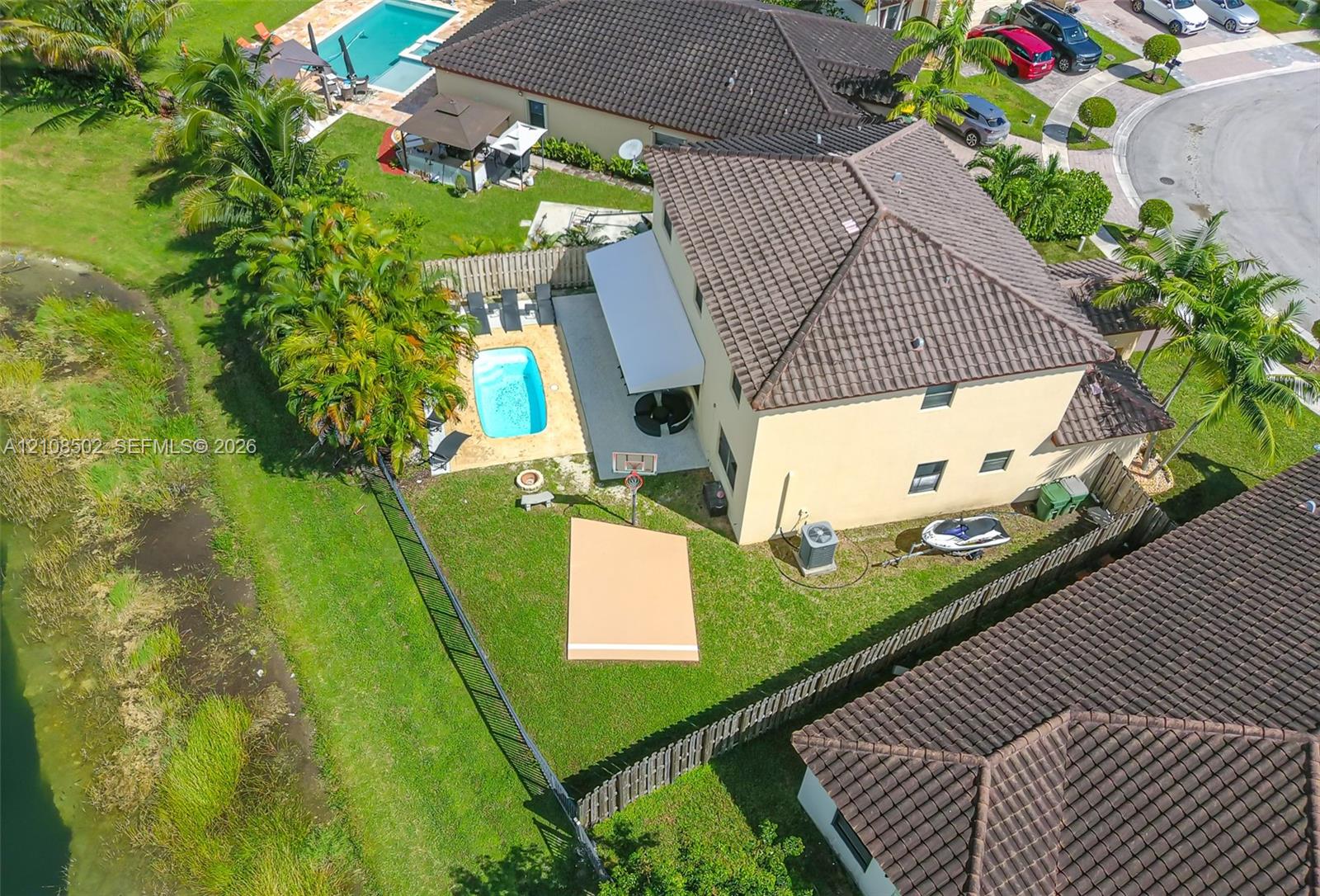 Aerial perspective featuring a tile roof, private swimming pool, concrete patio, and fenced backyard with water frontage
