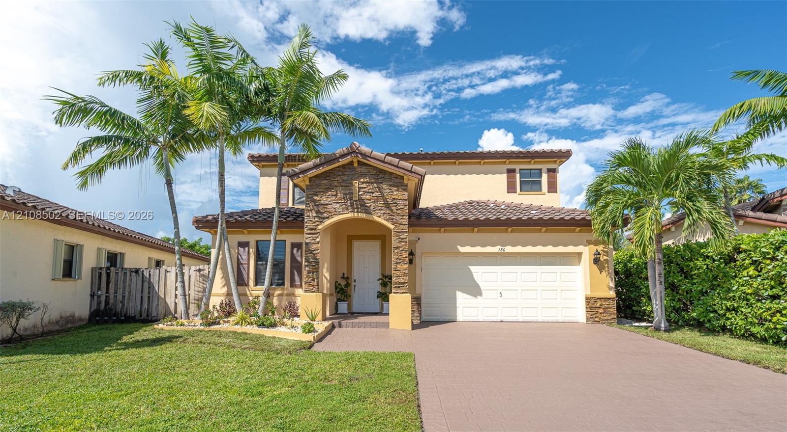 Two-story residence featuring a tile roof, stone-veneer entryway, stucco exterior, attached garage, and paved driveway Two-story residence featuring a tile roof, stone-veneer entryway, stucco exterior, attached garage, and paved driveway