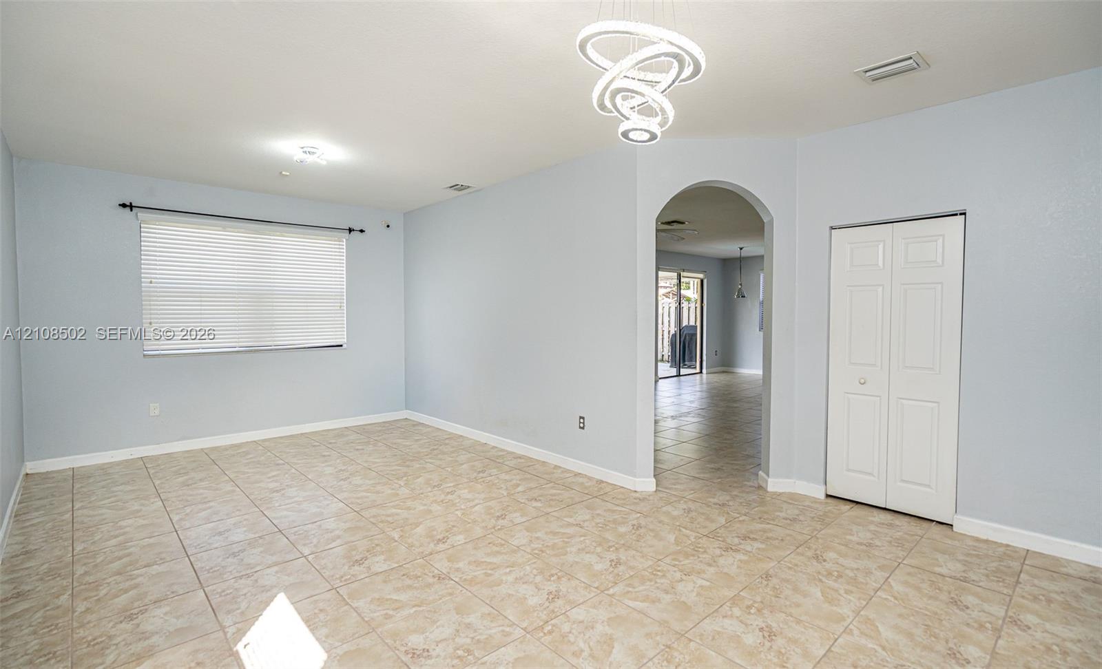 Interior space featuring tile flooring, modern sculptural LED chandelier, arched entryway, and double-door closet