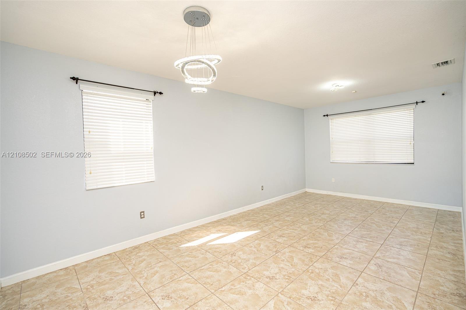 Interior space featuring ceramic tile flooring, neutral wall paint, modern multi-ring LED pendant lighting, and two windows with installed blinds