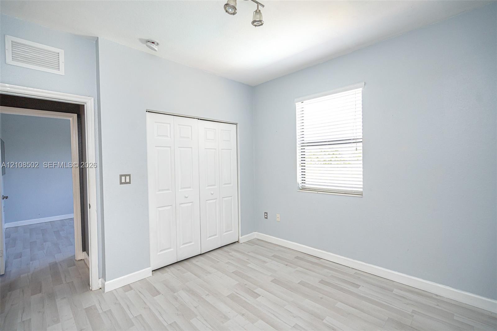 Room featuring wood-finish flooring, a double-panel closet with white doors, a single window with horizontal blinds, and a multi-bulb ceiling-mounted light fixture