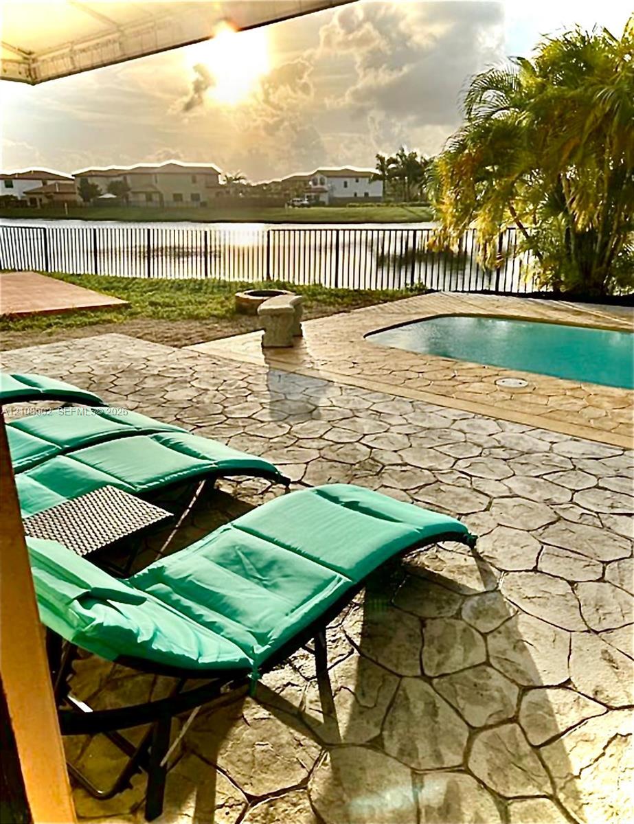Outdoor living area featuring a stamped concrete patio, in-ground swimming pool, metal perimeter fencing, and water frontage