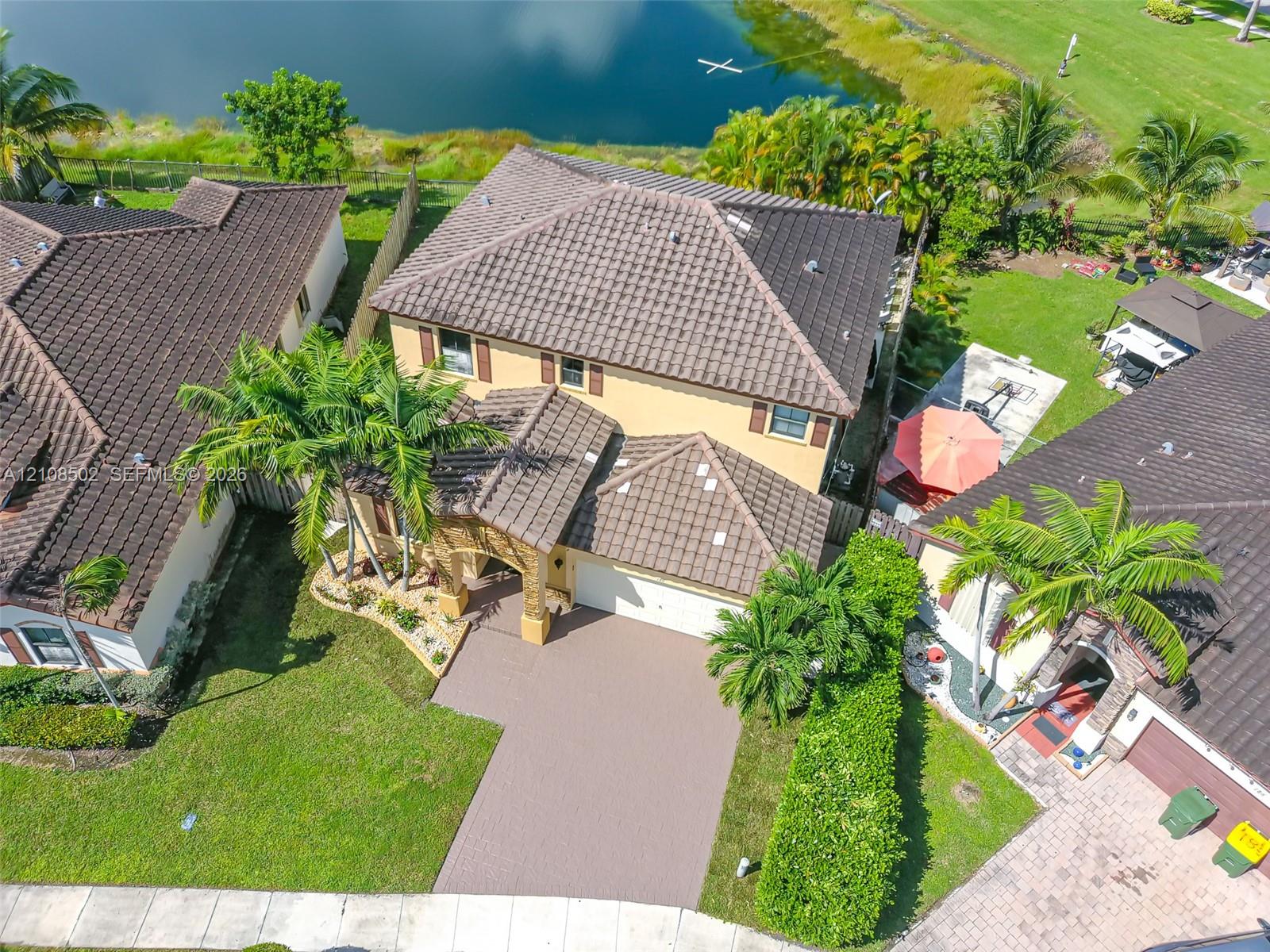 Two-story residence featuring a tile roof, paved driveway, arched entryway, and landscaped yard backing to a water feature