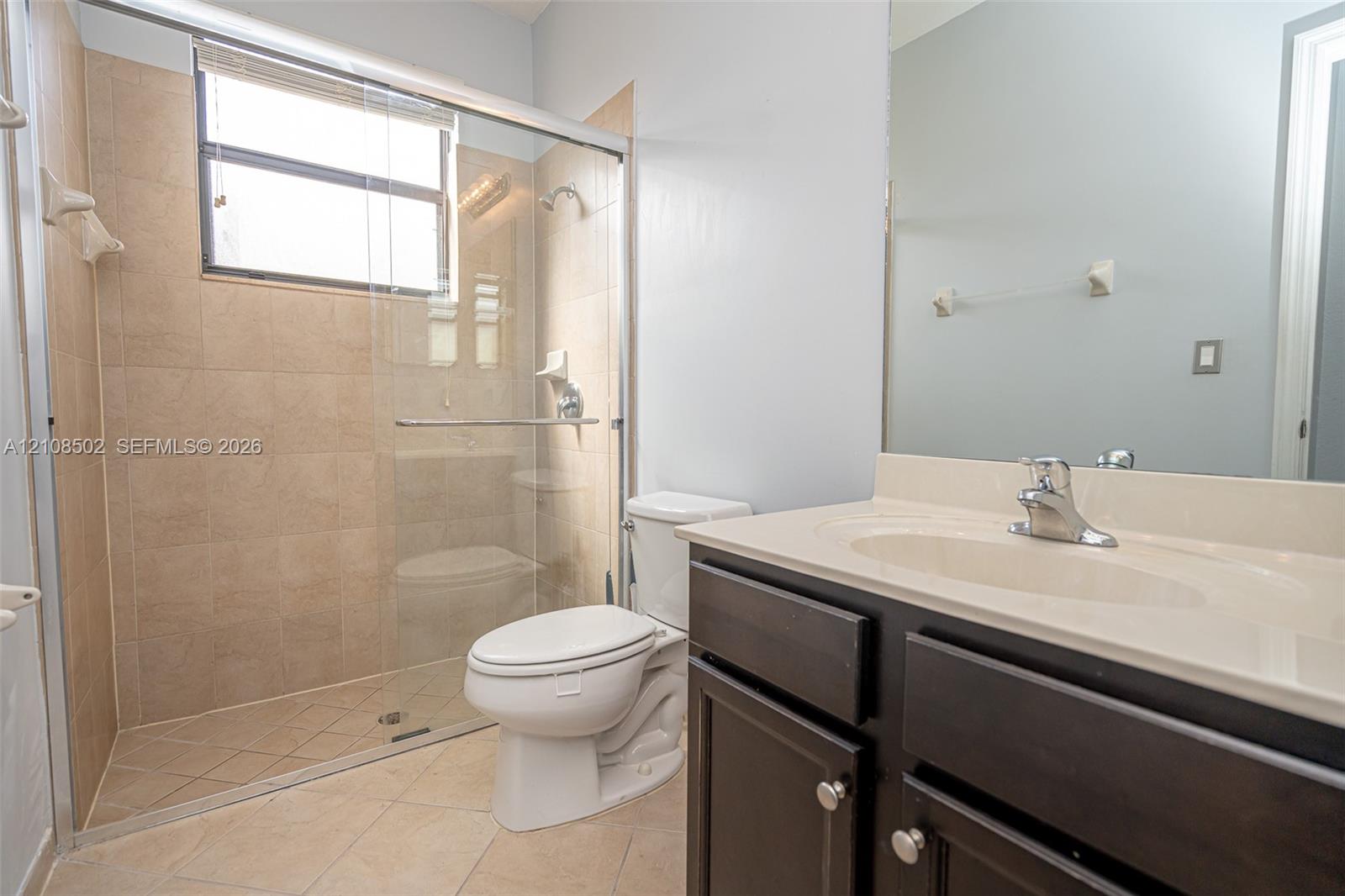 Bathroom featuring a dark wood vanity with a solid surface countertop, an undermount sink, a framed mirror, and a walk-in shower with a glass enclosure and tiled surround